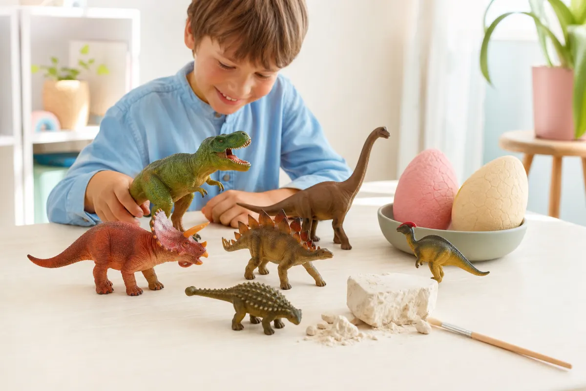 Generiska dinosaurieleksaker på ett ljust bord: figurer, kläckägg och utgrävningskit